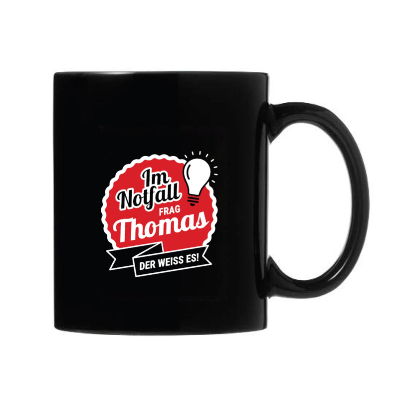 Schwarze Keramiktasse mit rotem und weißem Spruch 'Im Notfall frag Thomas, der weiß es!